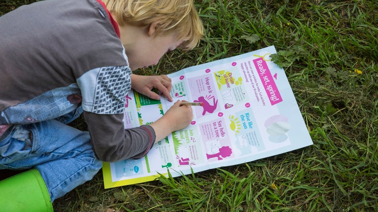 Image of a child wearing wellington boots, kneeling on grass, completing their Easter trail sheet